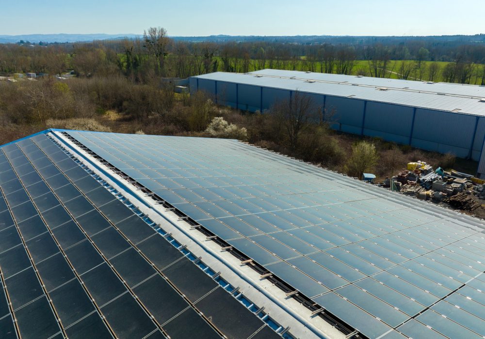 Aerial view of solar power plant with blue photovoltaic panels mounted on industrial building roof for producing green ecological electricity. Production of sustainable energy concept.